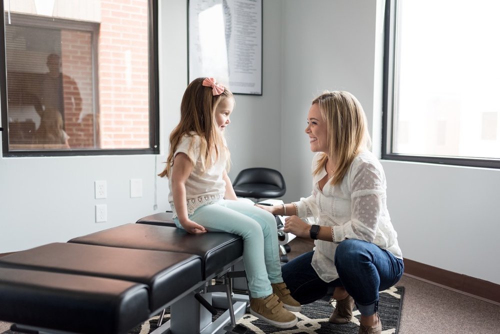 Brand photo of woman chiropractor meeting with a child sitting on her adjusting table at her chiropractor office in Franklin, TN.